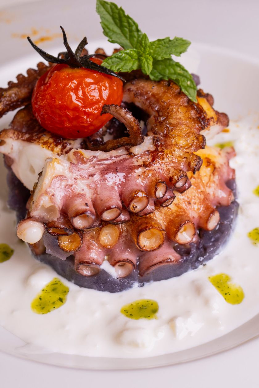 Polpo cotto alla brace e servito su una crema al latte con gocce di pesto di basilico in un ristorante elegante